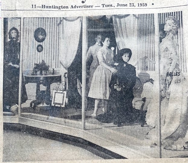 The dress at extreme left in the window is in a mulberry silk party dress trimmed with velvet. Second from left is a silk street dress. At right is a brocade silk dress trimmed with satin.